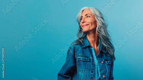 Mujer madura sonriendo con el pelo blanco y mirando de reojo sobre fondo azul photo
