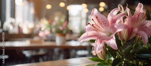 A beautiful bouquet of pink lilies, a type of flowering plant, is elegantly displayed on a wooden table in a cozy restaurant setting photo