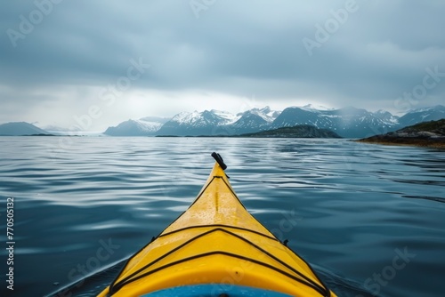 A yellow kayak glides through the tranquil arctic sea, with majestic snow-capped mountains as a backdrop. © Philipp