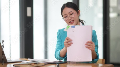 Asian businesswoman working with digital laptop computer and document management at desk in office.