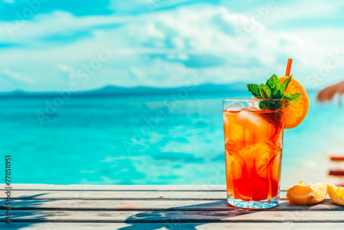Stunning orange tea in a tall glass garnished with citrus against clear blue ocean for a holiday scene