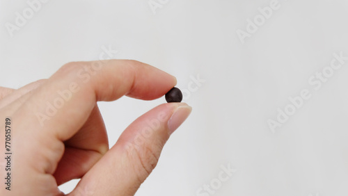 Fingers holding a small black ball, which is a traditional form of Chinese medicine. With copy space on the right.