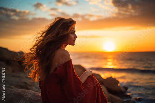 Young longhaired woman gazes at sunset over the sea, attractive, sensual pose, side view, warm golden hour colors photo