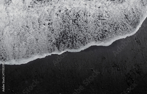 Foto The gentle ebb and flow of ocean waves caress the dark expanse of black sand along the shoreline