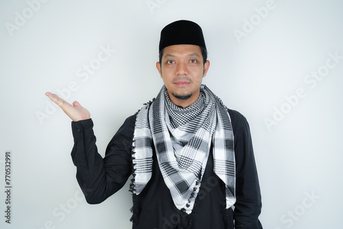 Cheerful handsome Asian Muslim man wearing Arab turban sorban pointing hand finger at empty space for advertising on isolated background photo