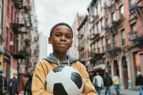 Young boy with a soccer ball smiling confidently on an urban street.