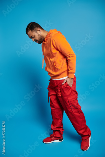 young african american man in vibrant outfit looking on floor against blue background