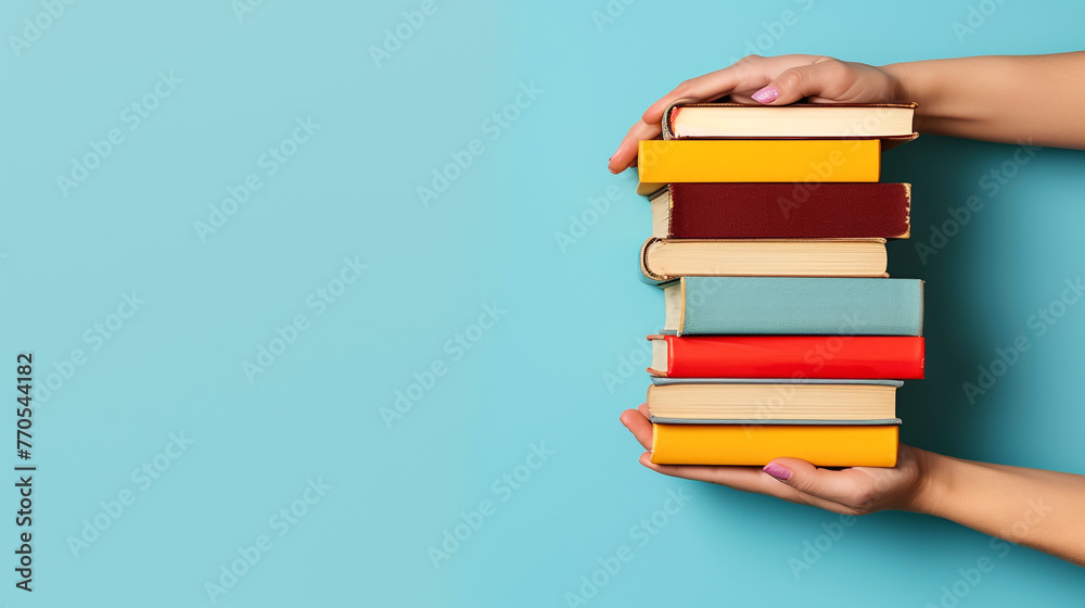 A woman's hand holding a stack of books against a blue background - obrazy, fototapety, plakaty 