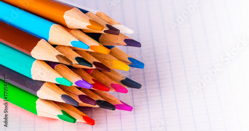 Group of multicolor pencils on white checkbook in a cage , close up shot
