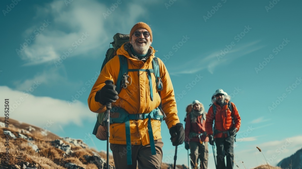 Happy senior man in a yellow jacket trekking in the mountains with a group of hikers behind him