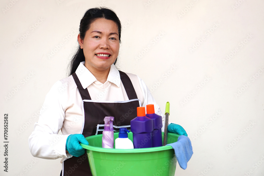 Asian woman housewife wears gloves, apron, holds bucket, bottles of cleaning liquid, alcohol spray, sanitary products and equipment for cleaning. Concept, Cleaning time for hygiene. Housekeeping. Asian woman housewife wears gloves, apron, holds bucket, bottles of cleaning liquid, alcohol spray, sanitary products and equipment for cleaning. Concept, Cleaning time for hygiene. Housekeeping.