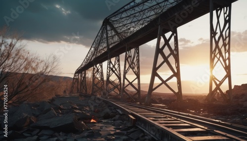 The twilight sky paints a quiet backdrop for the towering metal girders of a disused railway bridge. A lone campfire flickers, a small yet poignant contrast to the silent, imposing structures. AI