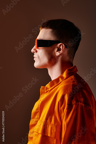 Side view fashion portrait of handsome man in orange shirt and sunglasses on brown background
