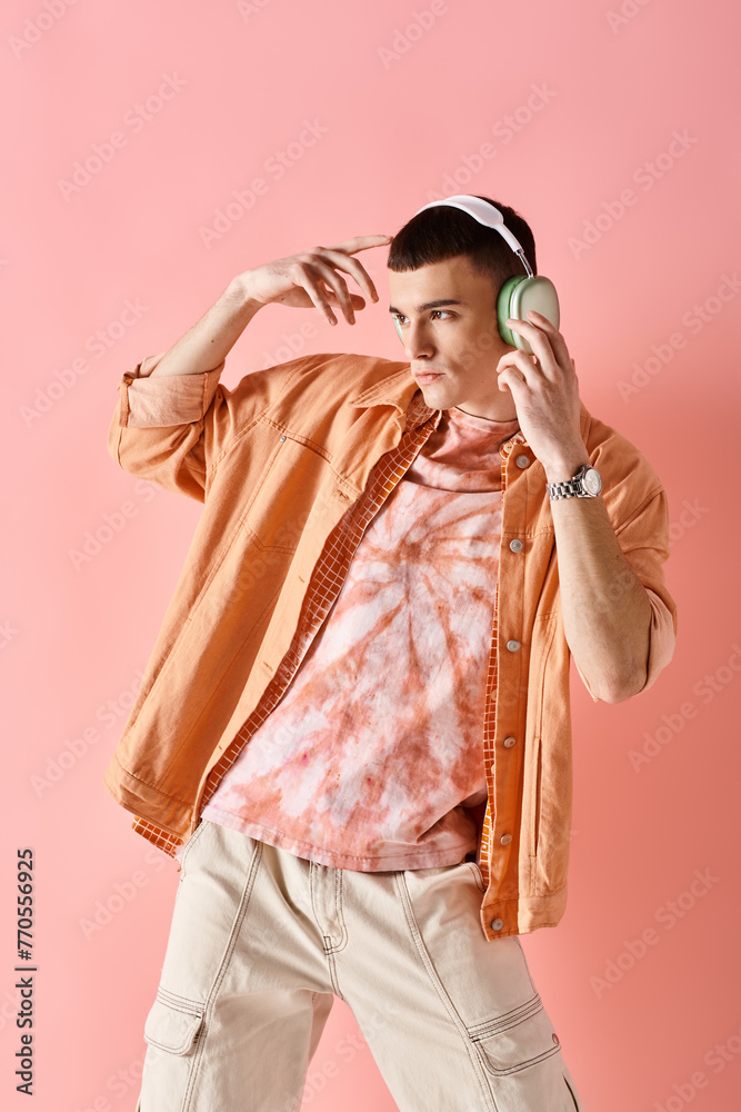 Fashionable man in layered outfit with wireless headphones dancing to music on pink backdrop Fashionable man in layered outfit with wireless headphones dancing to music on pink backdrop