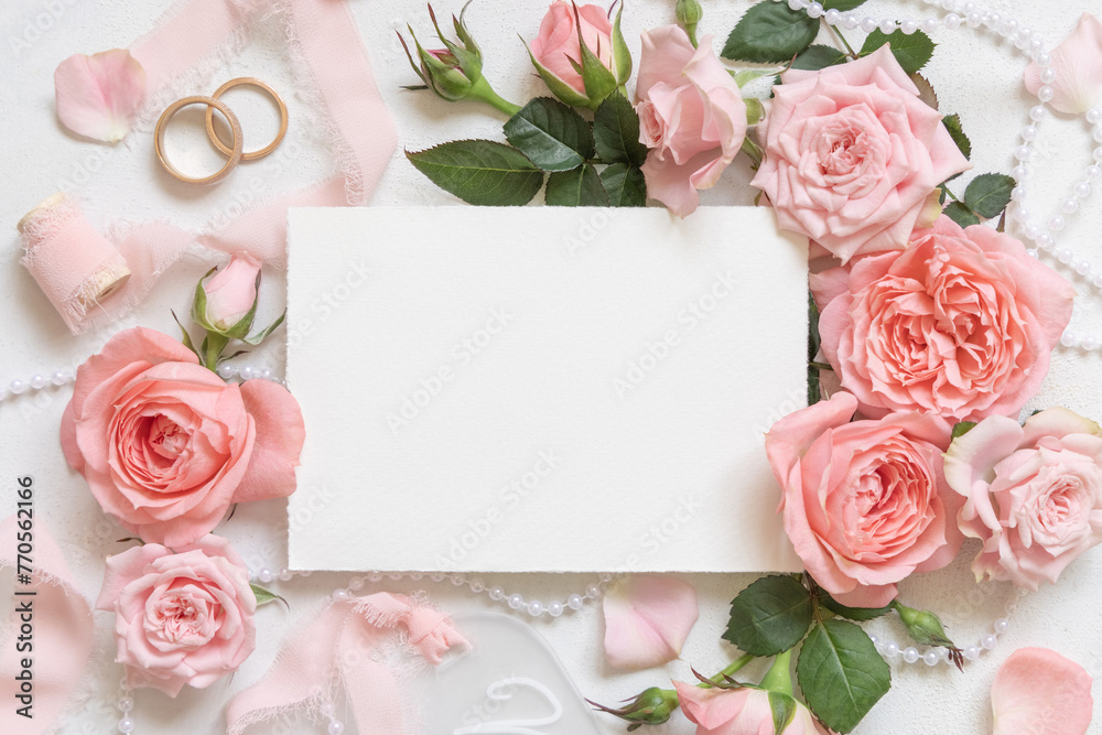 Blank card near pink roses, wedding rings and silk ribbons top view, wedding mockup