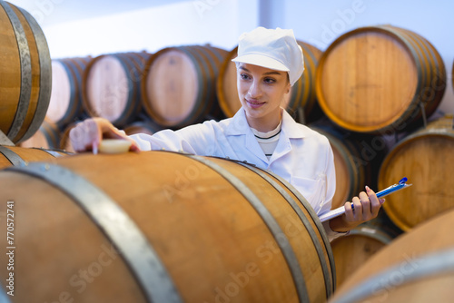 Canvas Print A wine industry quality control expert attentively inspects oak barrels in a cellar, ensuring the finest wine production standards