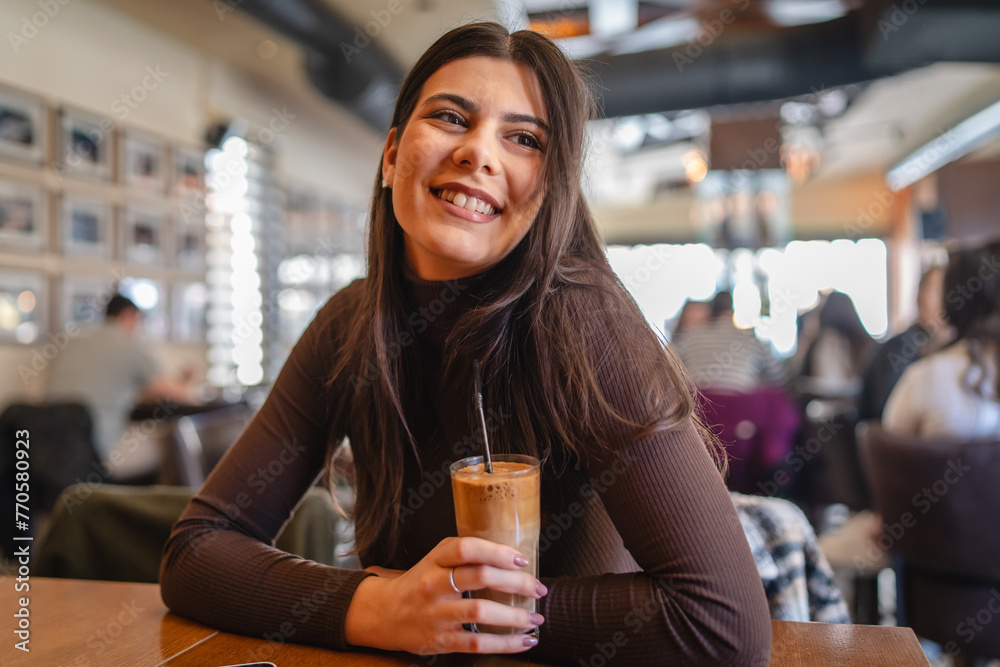 A one young happy girl or woman is drinking cold coffee in cafe or restaurant while using her phone to send messages
A one young happy girl or woman is drinking cold coffee in cafe or restaurant while using her phone to send messages