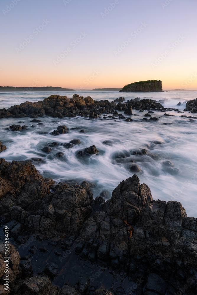 Wave flowing into the rocky coastline and island in the distance.
