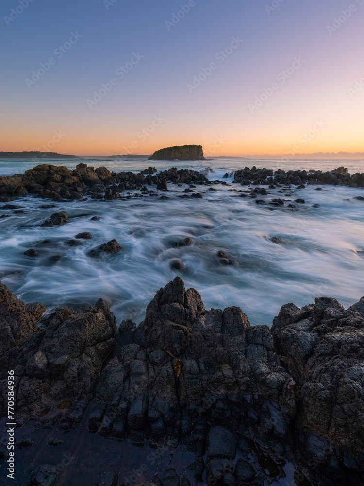 Wave flowing into the rocky coastline and island in the distance.