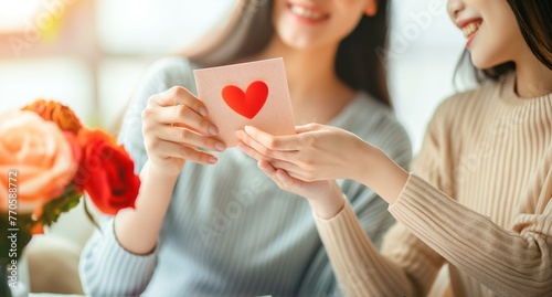 Two women are holding a card with a heart on it. One of the women is holding the card in her hand and the other woman is looking at her