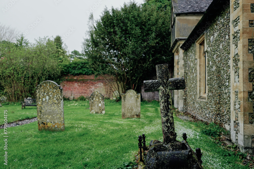 Shallow focus of an ornate stone crucifix shaped headstone seen in a medieval cemetery in England. Seen after a heavy storm.