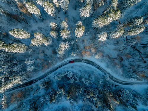 Aerial view of a car driving through a snowy forest in a winter scene.