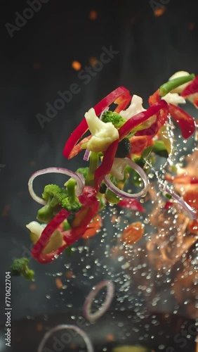 Closeup of chef preparing and throwing vegetable mix on frying pan on fire. Preparation fresh appetizing food. Vegetables flying in slow motion. Healthy vegetarian food cooking. Vertical video