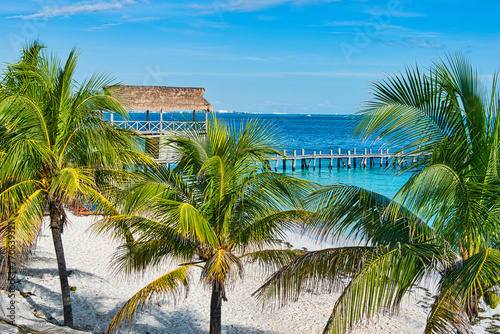 ISLA MUJERES ISLAND, MEXICO - DECEMBER 2021: The white sand beach with umbrellas, bungalow bar, boats, birds, and cocos palms, turquoise caribbean sea, Isla Mujeres island, Caribbean Sea, Cancun.  © Scotts Travel Photos