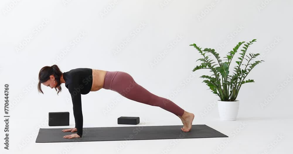 Athletic woman performs transitions from Chaturanga Dandasana exercise, plank pose to Adho Mukha Svanasana exercise, downward facing dog pose, practicing yoga on a mat in a bright room