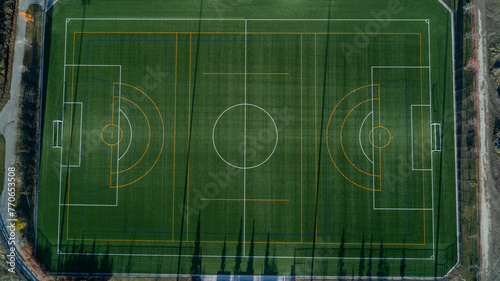 An aerial view of a green soccer field with lights and a path around it at sunrise