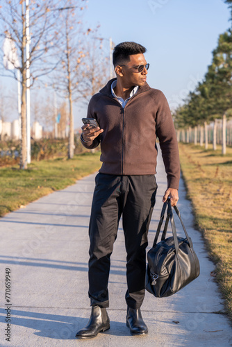 Obraz na plátně A man in a brown jacket and black pants is walking down a sidewalk while holding a black bag
