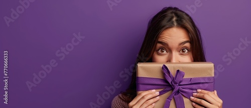 Mystery Present: A woman peeks curiously into a wrapped box, a playful smile on her face, against a deep purple background. Copy space sparks.