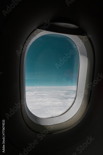 Airplane window offering a stunning view of the sky and white fluffy clouds below.