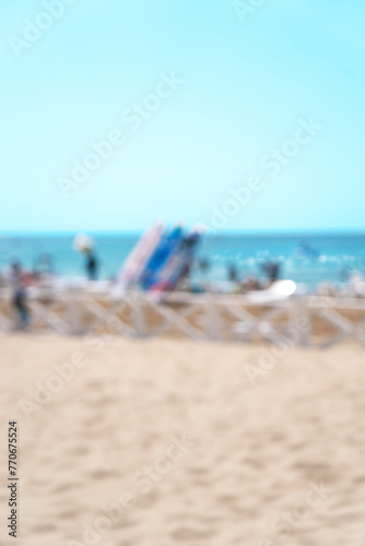 Blurred beach with blue sea and resting people on summer day. Abstract background of coastline with surfing and supboard. Vacation, travel