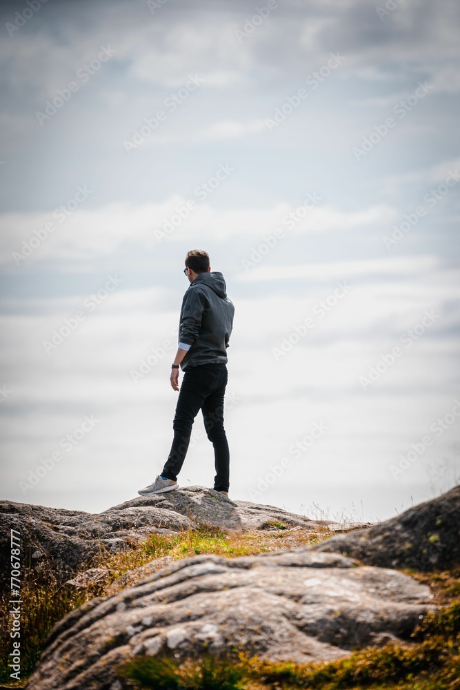 Young adult male hiker on a cliff under a cloudy sky in the countryside