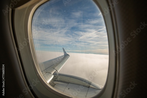 Airplane wing with clouds in the background seen through a window