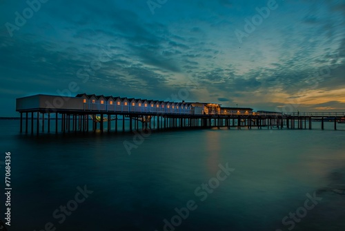 Tranquil night scene depicting a pier and buildings illuminated against a vibrant evening sky.