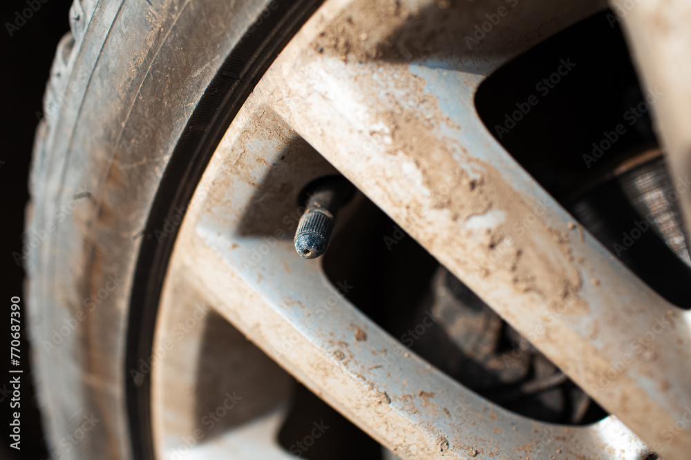 Close-up of tire valve cap on dirty car tire.