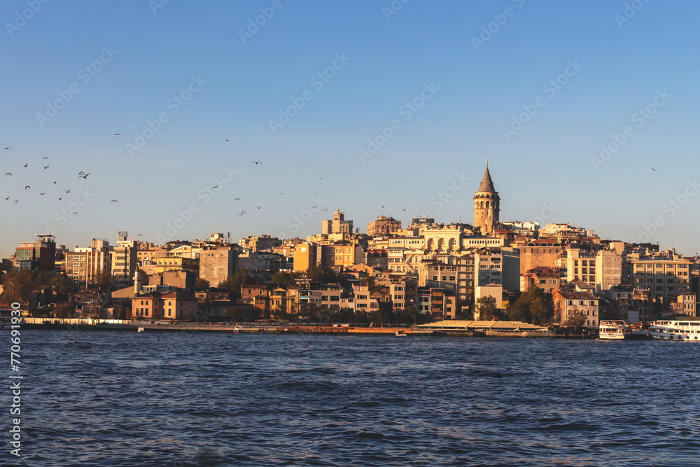 Galata Tower and Golden hhorn as seen from Eminonu pier, Istanbul skyline, birds in flight, soft evening light, clear blue waters
