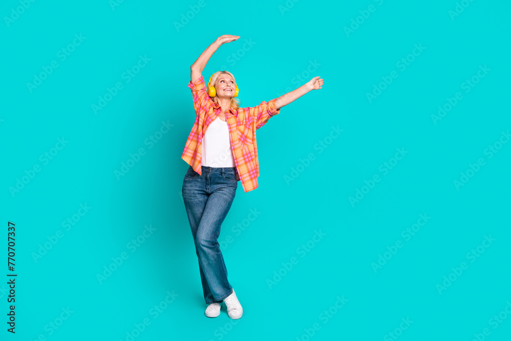 Full size photo of optimistic person dressed checkered shirt listen music in headphones look empty space isolated on teal color background Full size photo of optimistic person dressed checkered shirt listen music in headphones look empty space isolated on teal color background