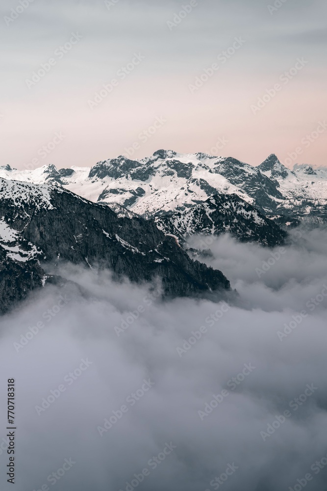 Scenic view of snow-covered mountains surrounded by a blanket of fog and clouds in a cloudy sky