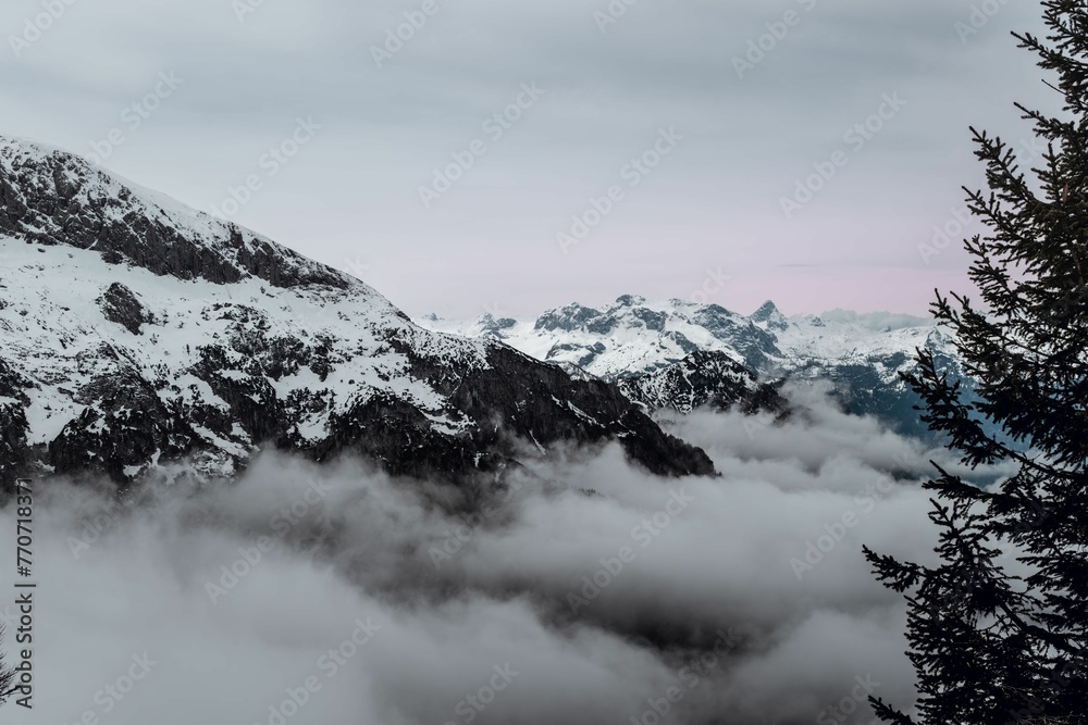 Snow-covered mountain peak with white wispy clouds hovering around its peak in Berchtesgaden