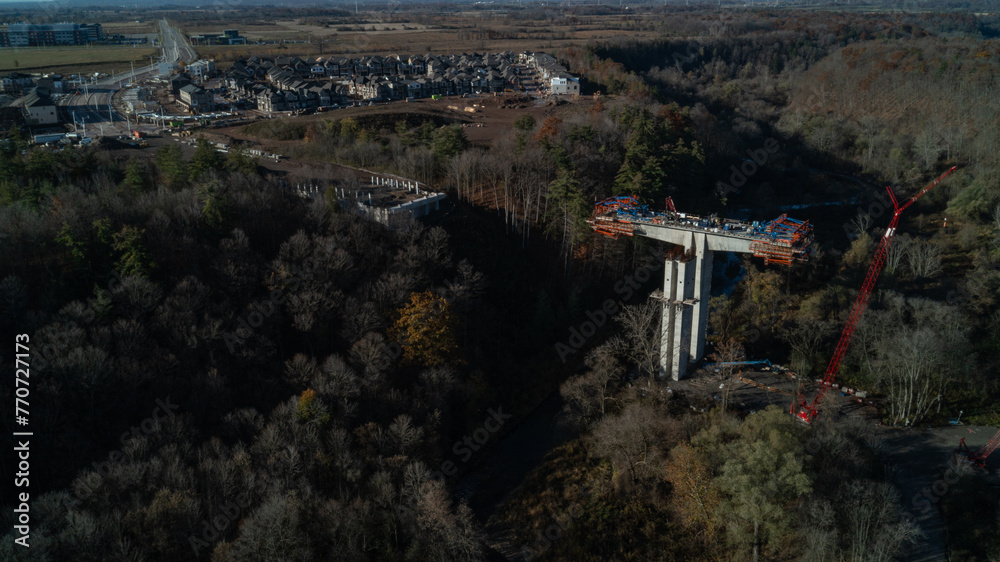 An aerial view of a bridge being built over a valley with a river and Forest in the fall