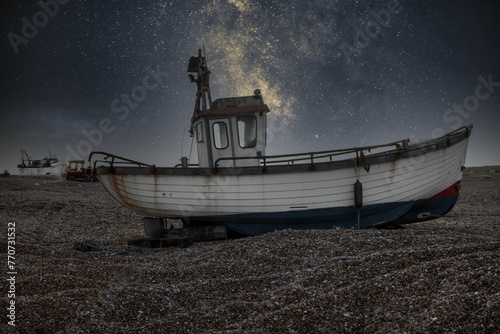 Old boat abandoned on a gloomy seaside beach under a starry night sky