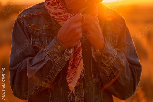 Close up of a cowboy adjusting a red bandana during a golden hour sunset