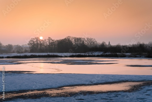 Beautiful winter sunset over a snow-covered landscape with trees in the background © Wirestock