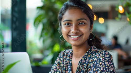 Portrait of a smiling young Sri Lankan woman with black hair seated and working on her laptop photo