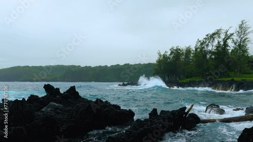 Black lava rocks beach at Keanae Penisula in Maui island. Waves splash on jagged black lava rocks on a cloudy day.  photo
