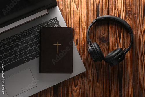 Bible book with laptop and headphones on a wooden table. Online Bible study