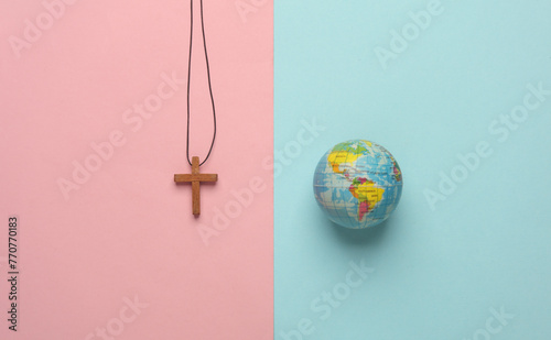 Wooden Christian cross on a string with globe on pink blue background. Messianism, Christian religion photo
